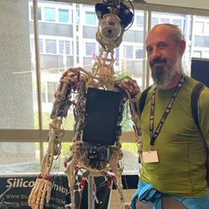 Samuel Jones profile image - Half length photo of Samuel standing next to a humanoid robot skeleton